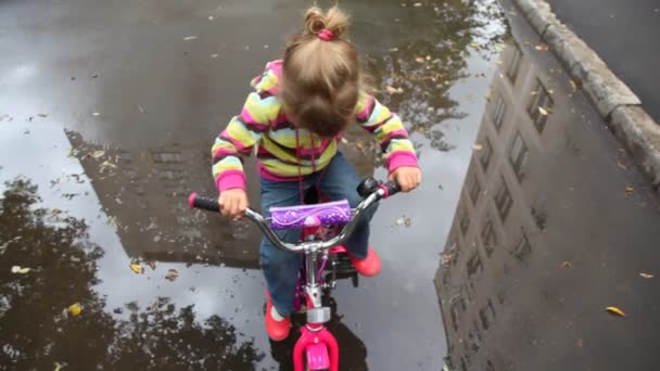 Talking little girl sits on bicycle on wet asphalt with puddles — Stock Video