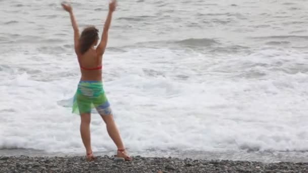 Young woman standing on pebble beach against waves of sea — Stock Video