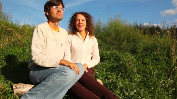 Paar zit op logboek op groene gazon en praat in park in de zomer — Stockvideo