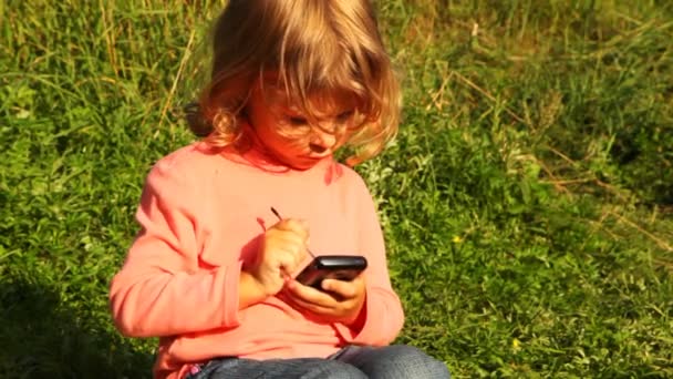 Girl sit in park, hold communicator in hands and play in it — Stock Video