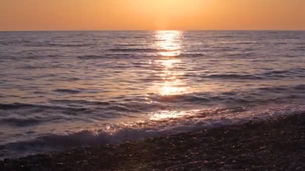 Young boy running on pebble beach, sunset sky and sea in background — Stock Video