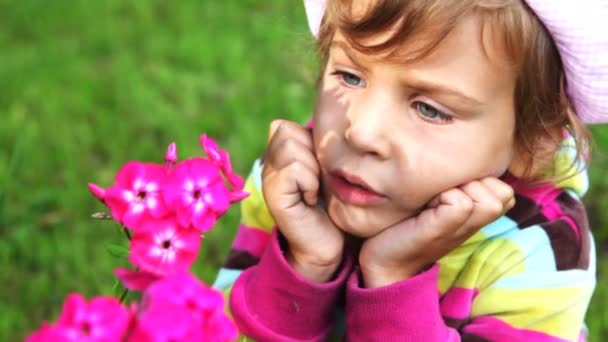 Liten flicka nära rosa blommor titt på nära håll och prata — Stockvideo