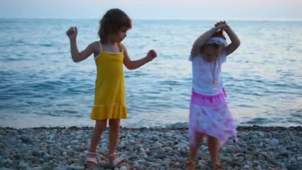 Two little girls dancing in evening pebble beach, sea in background — Stock Video