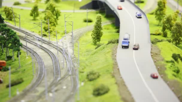 Пассажирский экспресс движется по железной дороге в современном игрушечном городе среди дорог с маленькими автомобилями и деревьями — стоковое видео