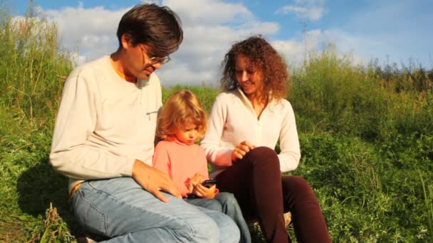 A família senta-se na colina verde, joga no comunicador. Prazo de validade — Vídeo de Stock
