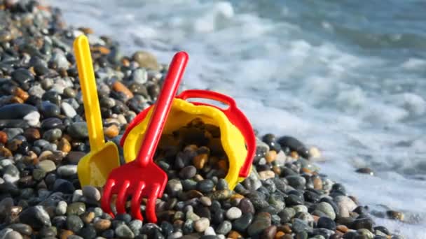 Cubo para niños amarillo con cuchara en la costa de guijarros — Vídeos de Stock