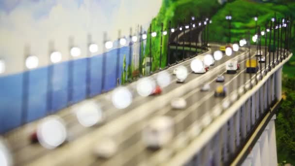 Close up toy bridge with automobile cars, buses and trucks stand on it before drawn panorama of sea and hills — Stock Video