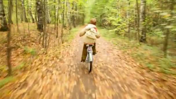 Камера рухається після того, як хлопчик їде на велосипеді в осінньому парку — стокове відео