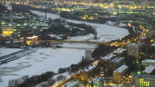 The top view on a winter city, on centre the frozen river. Gradually darkens. Time lapse. — Stock Video