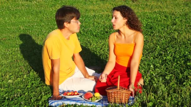 Kadın ve erkek birlikte yeşil çimenlerin üzerine oturur ve gülümseme ve meyve yiyor — Stok video