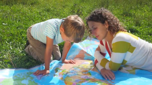 Young woman with boy sitting on green grass, looks at political map — Stock Video