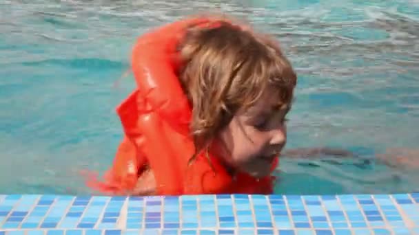 Onnellinen pieni tyttö pukeutunut puhallettava takki ui uima-altaassa — kuvapankkivideo