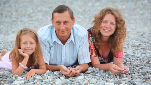 Familia feliz de tres personas acostadas en la playa de guijarros y hablando — Vídeo de stock