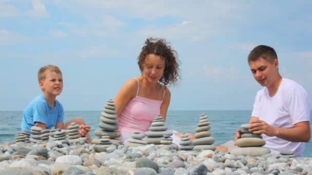 Familie gebouw pebble stapels op kiezelstrand, zee op achtergrond — Stockvideo