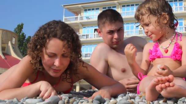 Familia digitación piedras en la playa de guijarros, hotel en el fondo — Vídeo de stock