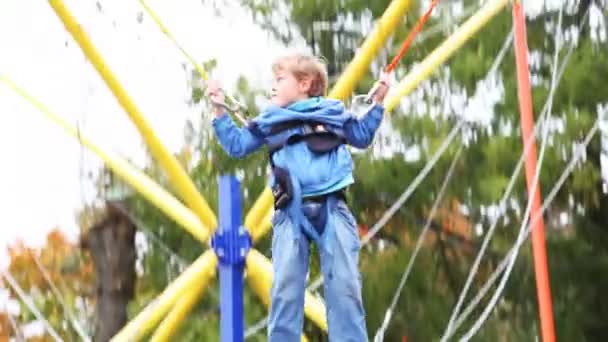 Niño tiembla suspendido por cordones de goma en la atracción del parque — Vídeos de Stock