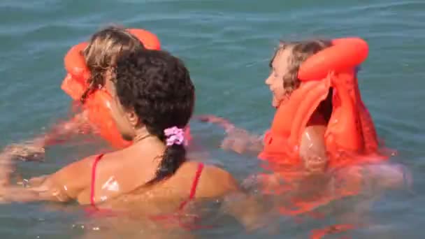 Jonge vrouw met twee kleine meisjes en jongen op opblaasbare matras heeft plezier in zee — Stockvideo