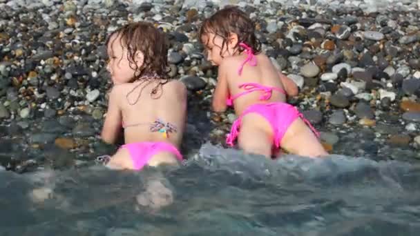 dvě šťastné malé holčičky, které leží na oblázkové pláži s mořem surfovat