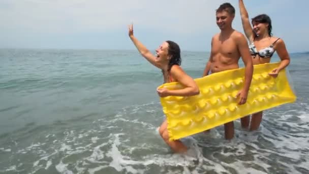 Дві жінки і чоловік тримає надувний матрац стоїть на пляжі — стокове відео