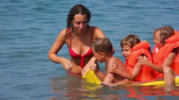 Молодая женщина с мальчиком и двумя маленькими девочками на надувной матрасе веселится в море — стоковое видео