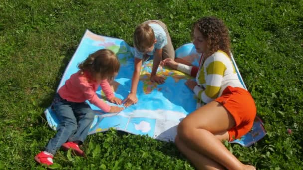 Young woman, boy and little girl sitting on green grass, looks at political map — Stock Video