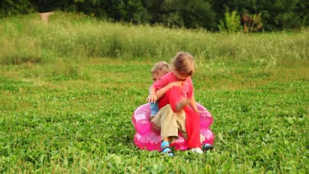 Ragazzo e ragazza giocano allo sciocco seduto su una poltrona gonfiabile per bambini sul campo nel parco — Video Stock