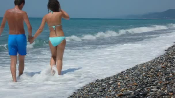 Uomo e donna in costume da bagno avendo unito le mani che camminano sulla costa del mare dalla fotocamera — Video Stock