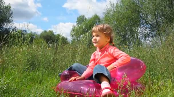 Niña linda se sienta en la silla inflable al aire libre en el parque de verano — Vídeos de Stock