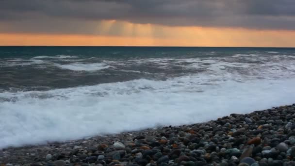雨の雲と夕焼け空の下の小石の海岸に海の波します。 — ストック動画