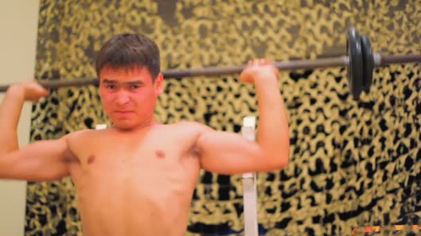 Jeune homme athlétique en salle de gym faisant haltérophilie assis sur un banc de musculation — Video