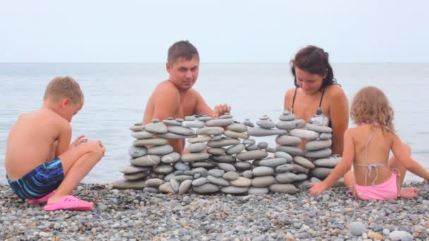 Famiglia di quattro costruzione muro di pietre sulla spiaggia, mare surf sullo sfondo — Video Stock