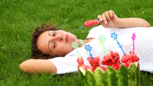 Young woman eating watermelon while laying on grass — Stock Video