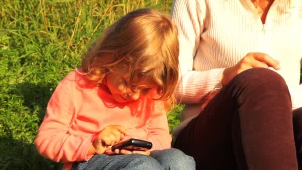 Filha e mãe senta-se gramado verde e jogar no comunicador — Vídeo de Stock