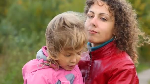 Joven mujer abraza pequeña hija en el viento al aire libre — Vídeos de Stock