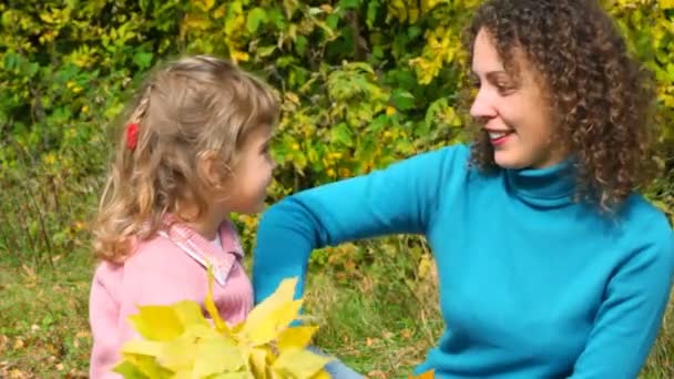 Mujer joven y niña jugando con hojas de otoño en el parque — Vídeos de Stock