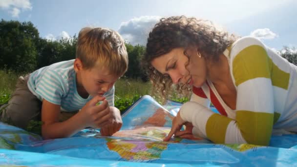 Jeune femme avec un garçon assis sur l'herbe verte, regarde la carte politique — Video