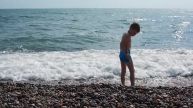 Çocuk deniz dalgaların arasında duran ve atma su çakıl taşı.