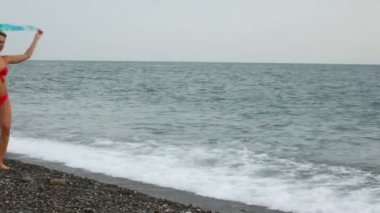Beach'te kameraya yürüyen ellerde kumaş ile bikini giymiş genç kadın