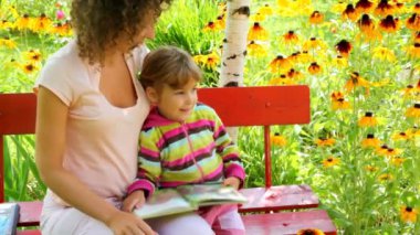 Anne ve kızı bahçede bankta kitap okumak