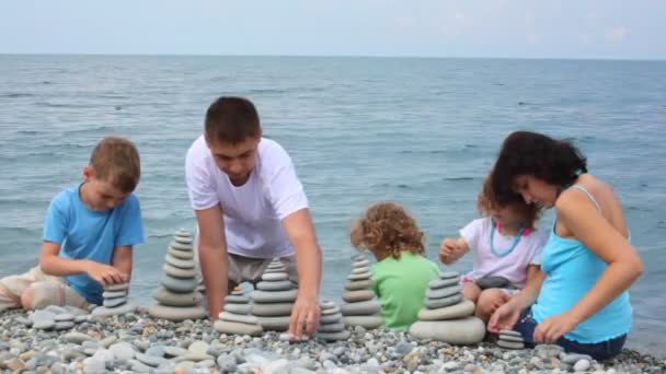 Familie gebouw steen stapels op kiezelstrand, zee op achtergrond — Stockvideo