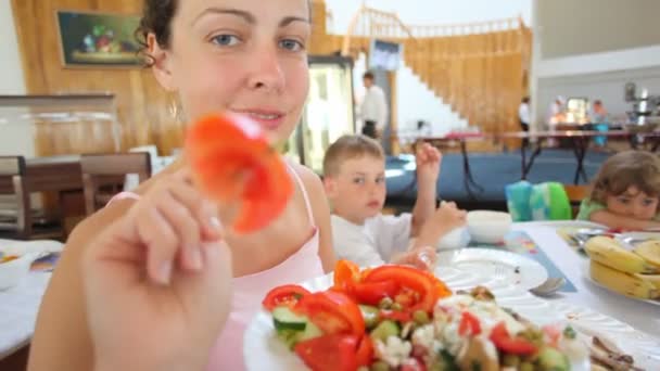 Улыбающаяся женщина приносит красный помидор на вилку на камеру в кафе — стоковое видео