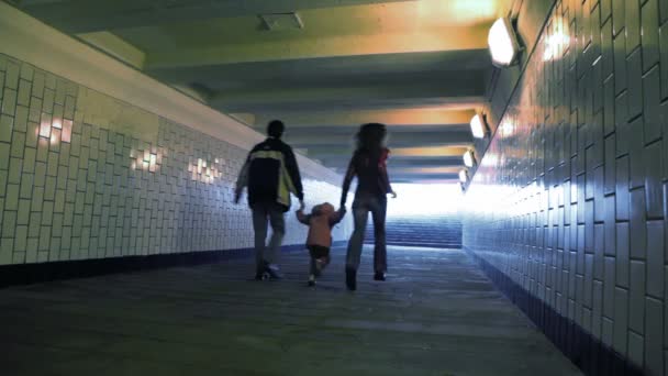 Family of three running in underground passage from camera, joined hands — Stock Video