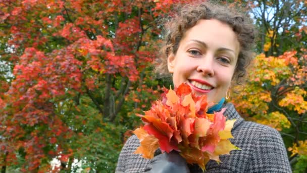 Портрет улыбающейся молодой женщины с осенними листьями в парке — стоковое видео