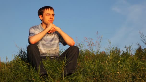 Young man easy sits on grass and deeply breathes in park in summer — Stock Video