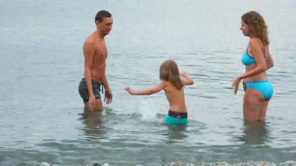 Dreiköpfige Familie, die im Meer steht und mit Wasser kokettiert, schließt euch zusammen — Stockvideo