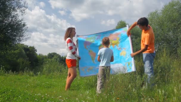 Hombre y mujer enrollando mapa político y dando a niño en parque de verano — Vídeos de Stock