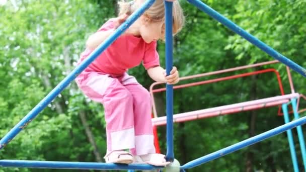 Malá dívka blondýnka v růžovém oblečení leze na železném prutu na dětském hřišti — Stock video