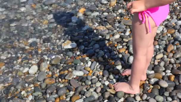脚的小女孩站在圆石滩附近海冲浪 — 图库视频影像
