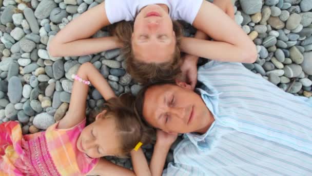 Happy family of three persons lying on pebble beach, top view — Stock Video