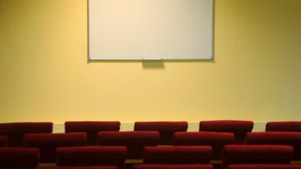 Conference hall with whiteboard on wall and red chairs, panning downwards — Stock Video